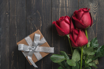 Bouquet of red rose flower and present box on dark wooden table. Can use for valentine day concept or background.