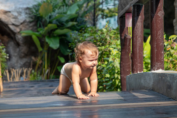 Child crawls along the dark brown wooden walkway of the bridge at sunset. Baby learn crawl on the background of greenery and a wooden bridge. There is a place for text.