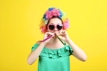 Young girl in clown wig and air whistle on yellow background