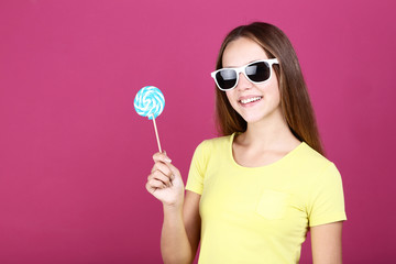 Young girl in sunglasses holding lollipop on pink background