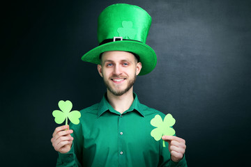 St. Patrick's Day. Young man wearing green hat with paper clover on black background