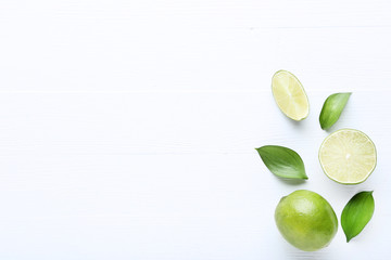 Ripe limes with green leafs on white wooden table