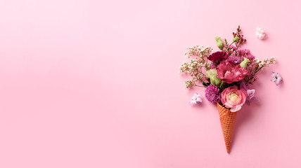 Summer minimal concept. Ice cream cone with pink flowers and leaves on punchy pastel background....