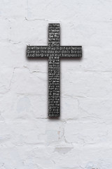 Black wooden cross with the Lord's prayer on white  brick wall with shabby stucco background