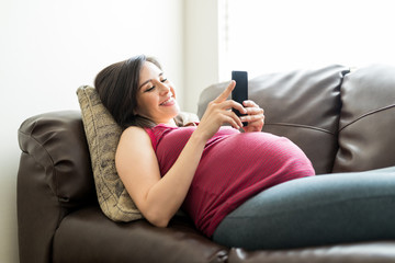 Expectant Woman With Mobile Phone Lying On Sofa