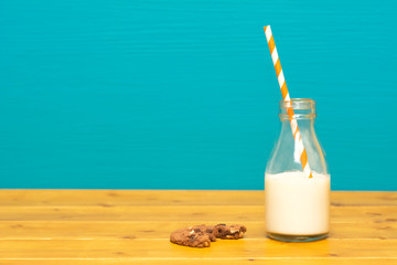 Straw and half full milk bottle with a half-eaten cookie