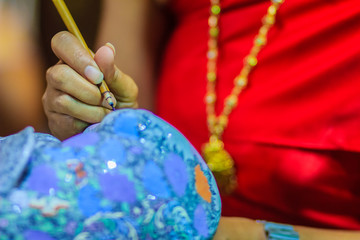 Fototapeta premium Close up Thai woman artist in red Thai style dressed is painting the masterpiece of Benjarong pattern, the famous 5- colored porcelain ceramic wares.