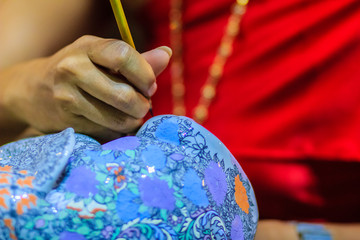 Close up Thai woman artist in red Thai style dressed is painting the masterpiece of Benjarong pattern, the famous 5- colored porcelain ceramic wares.