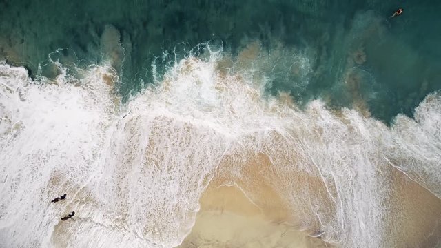 Aerial view of couple walking through turquoise waves on beach