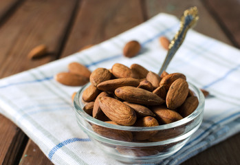 Almonds in a glass bowl on grained wood background. Selective focus.