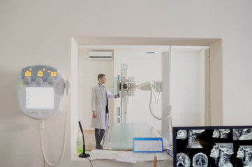 the picture of a male radiologist adjusting the X-ray machine behind the screen
