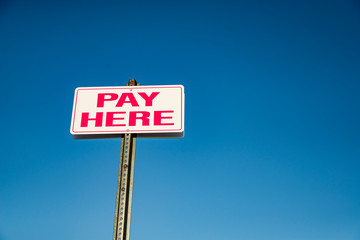 Pay Here signboard on top of an exterior wall with parked cars