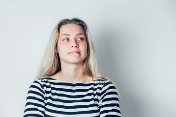 Close up indoor portrait of young dissatisfied woman biting lower lips on white background with copy space.