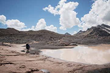 A mountaineer with a backpack walks in crampons walking along a dusty glacier with sidewalks in the...