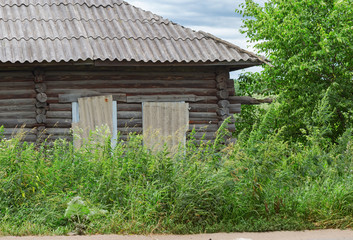 Fototapeta na wymiar Old wooden house overgrown with tall grass. Abandoned country house. Rural scene.