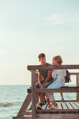 Happy smiling couple of young woman and man sitting on a pier over the sea during summer vacations