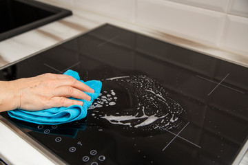 A woman's hand with a blue microfiber cloth rubs a glass ceramic stove in the kitchen.