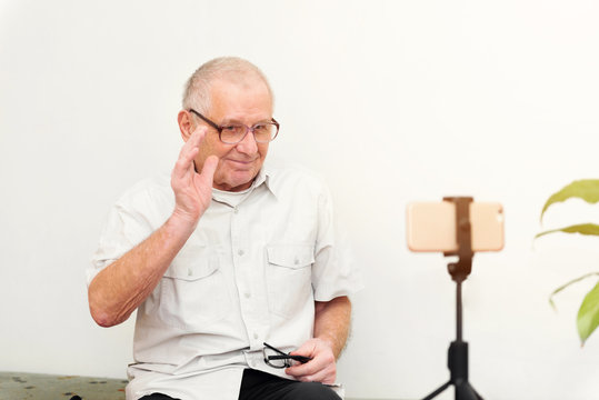 Smiling Eldery Man Looking At Camera Making Video Blog Or Call At Home Sitting On Sofa Dating Online Headshot