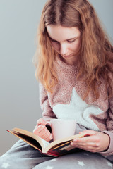 Girl enjoying the reading a book and drinking coffee at home