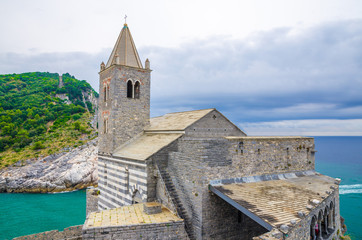 Fototapeta premium Chiesa San Pietro catholic church with bell tower, Lord Byron Parque Natural park, Palmaria island with green trees, cliffs, Portovenere, blue turquoise water Ligurian sea, La Spezia, Liguria, Italy