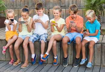 Group of smiling children playing with mobile phones outdoors