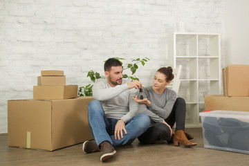 Loving couple sitting on the floor in their new house, smiling and looking at a key of their new property