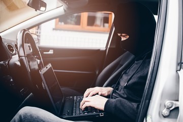 Masked thief hacker in a balaclava disarming car security systems