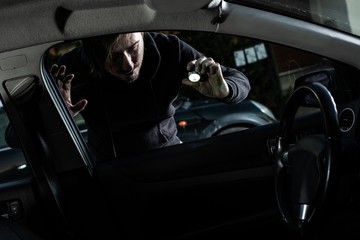 Masked thief in a balaclava looking to car interior