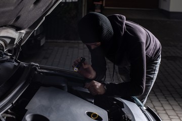Fototapeta na wymiar Thief in a balaclava with flashlight trying to steal a car