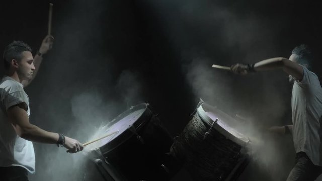Two people play on color drums on the black background