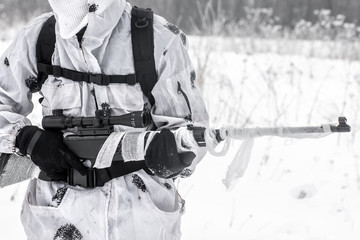 Man soldier in the winter on a hunt with a sniper rifle in white winter camouflage