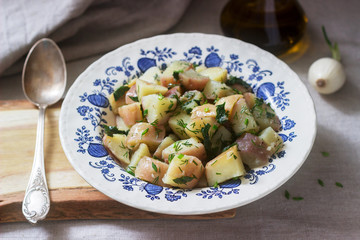 Traditional cold potato salad with onions and herbs on a linen tablecloth background. Rustic style.