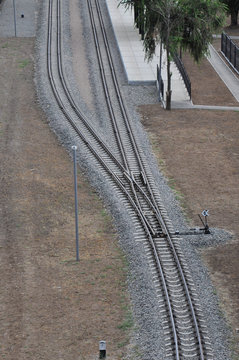 Aerial view of forking railway tracks with posts and tidy platform under green trees.