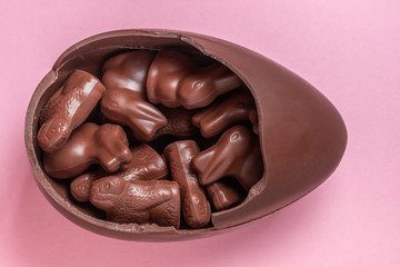 Easter bunnies and lambs in broken chocolate Easter egg over pink background, holiday concept