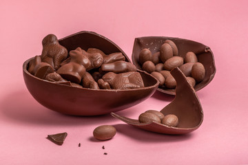 Easter eggs, bunnies and lambs in broken chocolate Easter egg over pink background