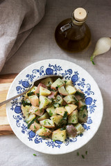 Traditional cold potato salad with onions and herbs on a linen tablecloth background. Rustic style.