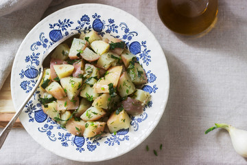 Traditional cold potato salad with onions and herbs on a linen tablecloth background. Rustic style.