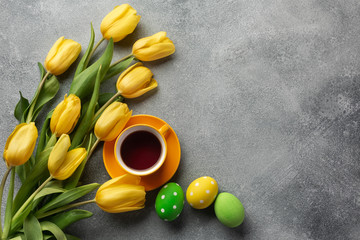 Easter background with blue, green eggs and a cup of tea in nest and yellow tulips. Top view with copy space