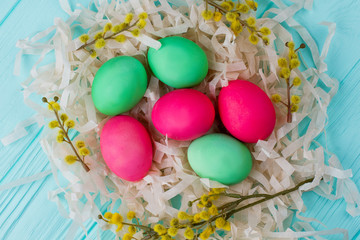 Close up Easter eggs in artificial nest. Colorful Easter eggs and pussy willow with catkins in nest from paper stripes. Easter festive design. Beautiful Easter composition.