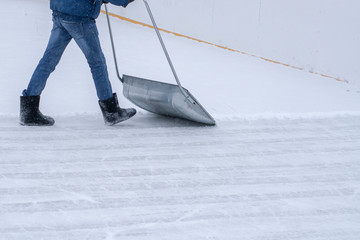Man cleans the ice rink with a big snow shovel