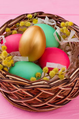 Colorful Easter eggs in wicker basket. Golden egg among colorful eggs in Easter woven basket. Symbol of happy Easter.