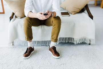 cropped view of senior man sitting on sofa and holding remote control