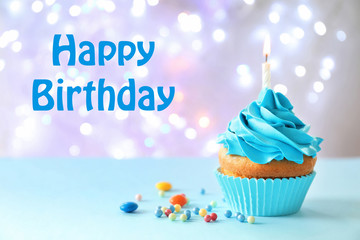 Delicious birthday cupcake with candle on table against blurred background