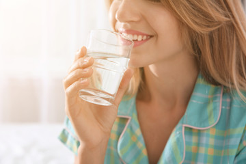 Young woman drinking water from glass indoors, closeup