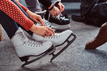 Young couple preparing to a skating. Close-up photo of their hands tying shoelaces of ice hockey...