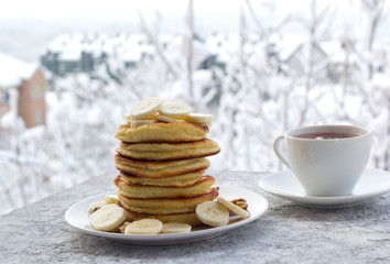 pancakes with honey, banana and nuts, a cup of tea, breakfast, view of the winter landscape