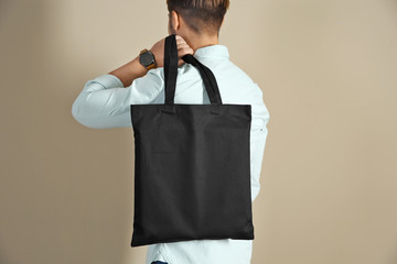 Fototapeta Young man holding textile bag on color background, closeup. Mockup for design obraz
