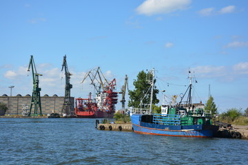 Old fishing trawler lies in the port of Danzig, Gdansk in Poland, cranes ships and industrial buildings in the background, summer with blue sky