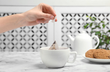 Woman brewing tea with bag in cup on table, closeup