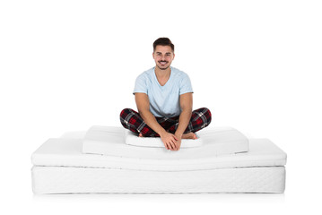 Young man sitting on mattress pile against white background